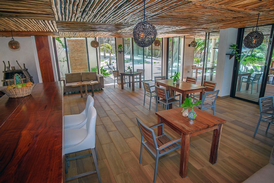 Interior of a beachside restaurant with wood floors, tables, and a natural, woven ceiling.