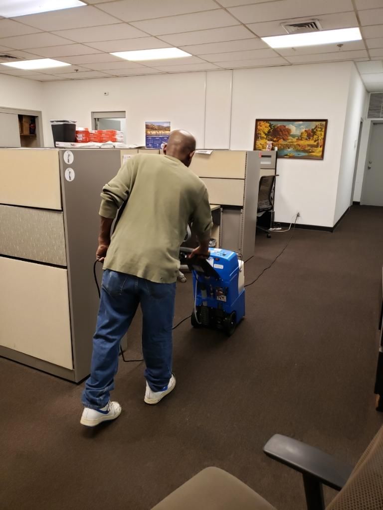 A man is cleaning the floor of an office with a vacuum cleaner.