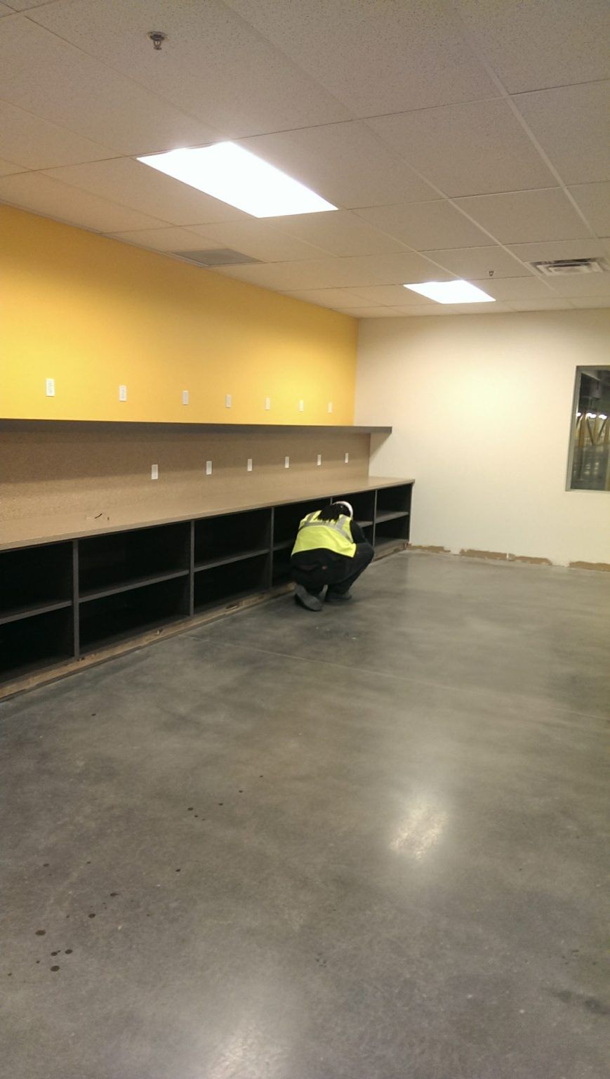 A man in a yellow vest is sitting on the floor in an empty room.