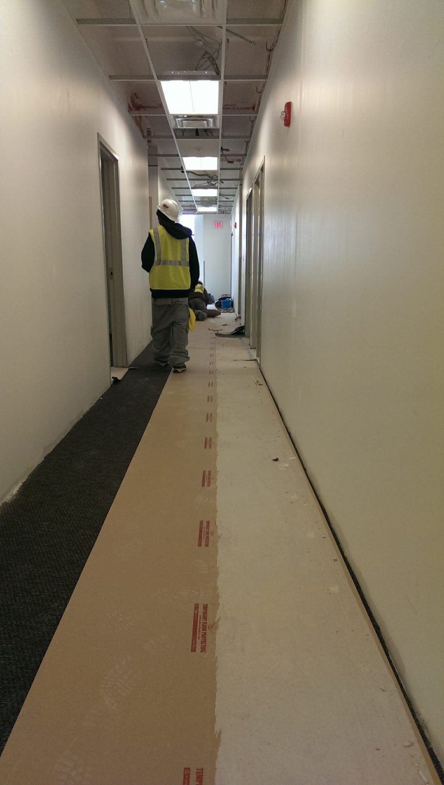 A man in a yellow vest is walking down a long hallway.