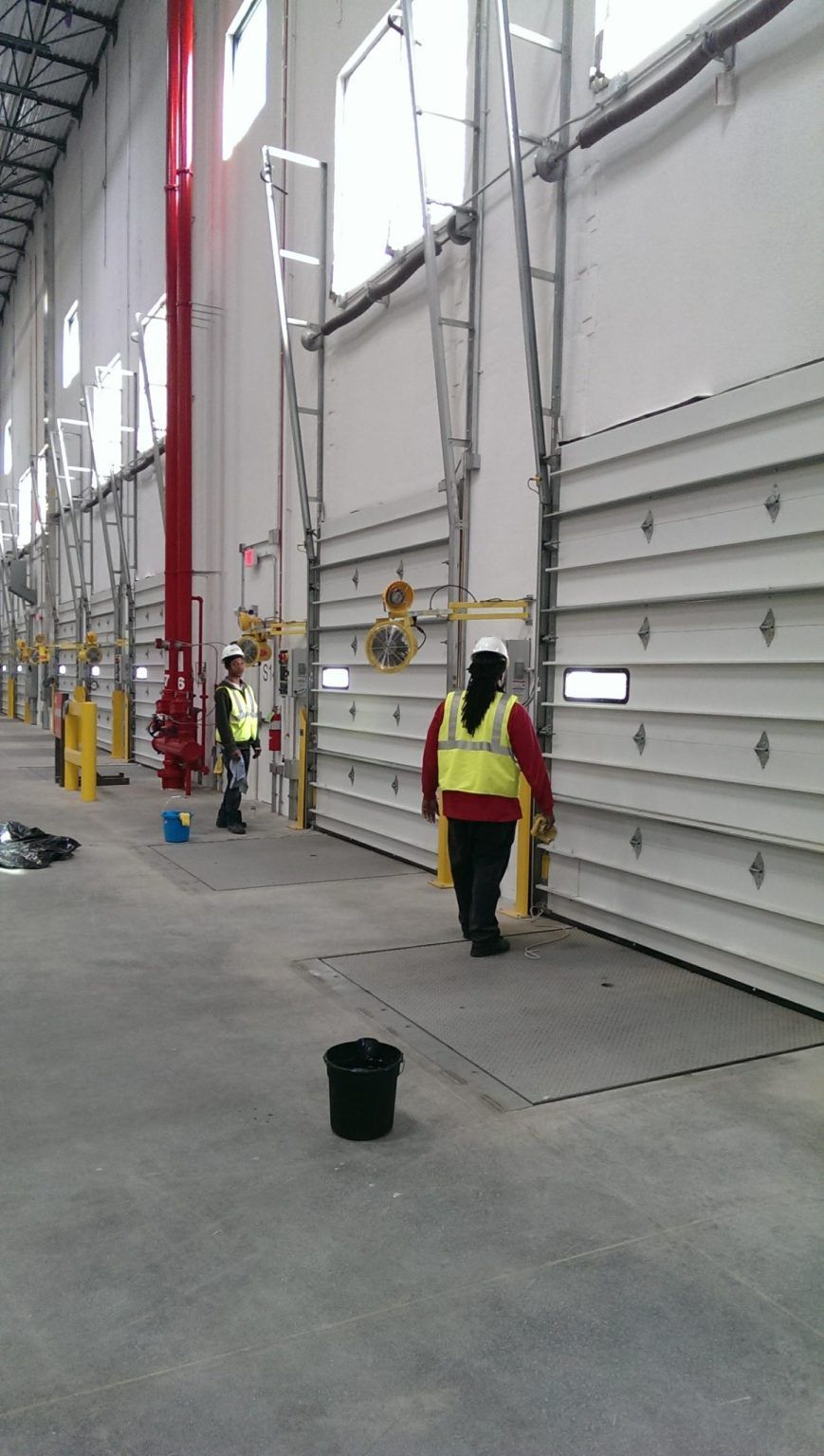 A woman in a yellow vest is walking through a large warehouse.