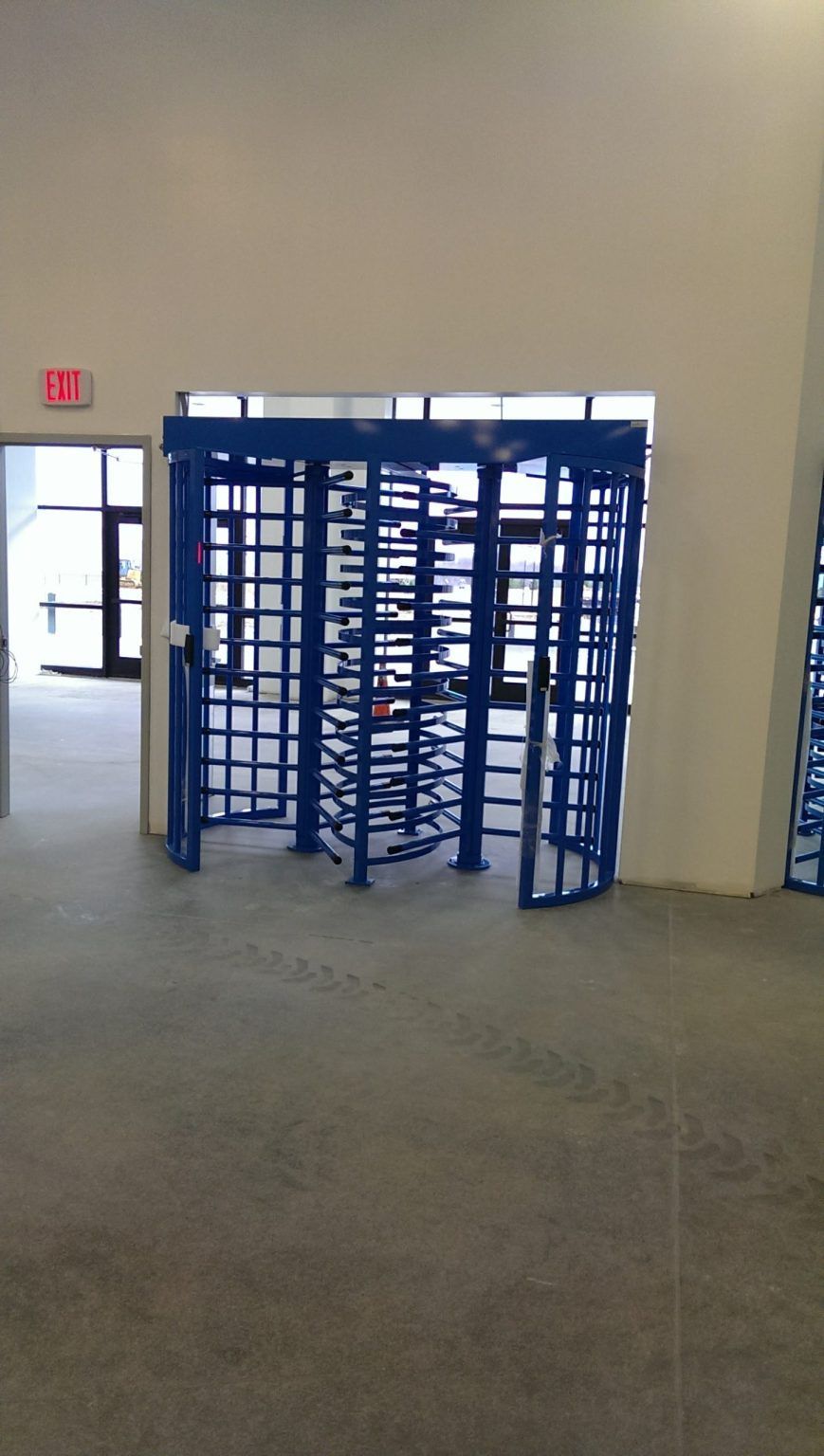 A blue turnstile in an empty room with a red exit sign