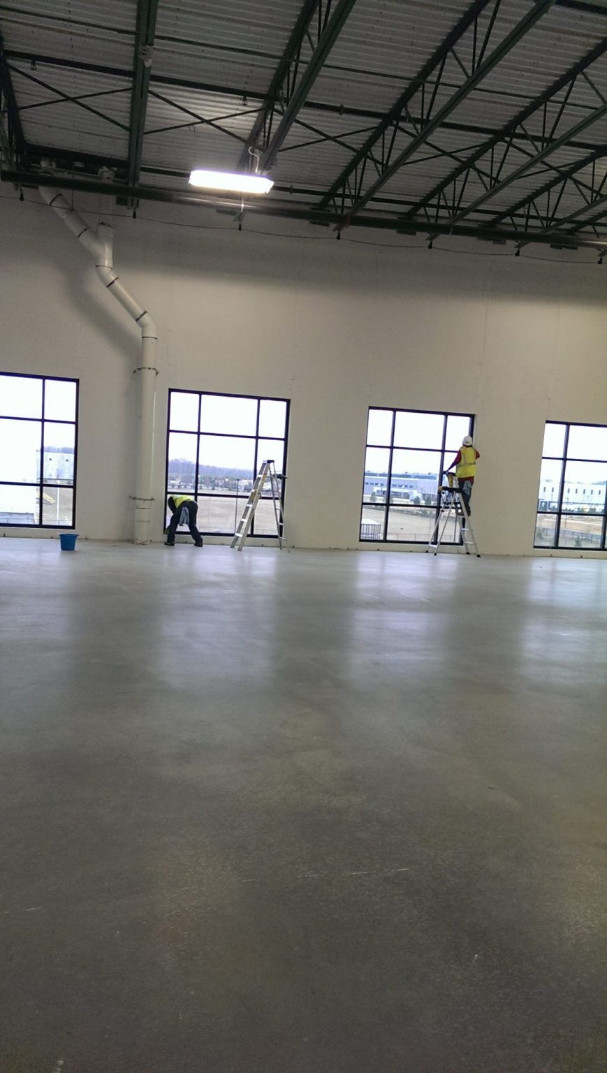 A man is standing on a ladder in a large room with lots of windows.