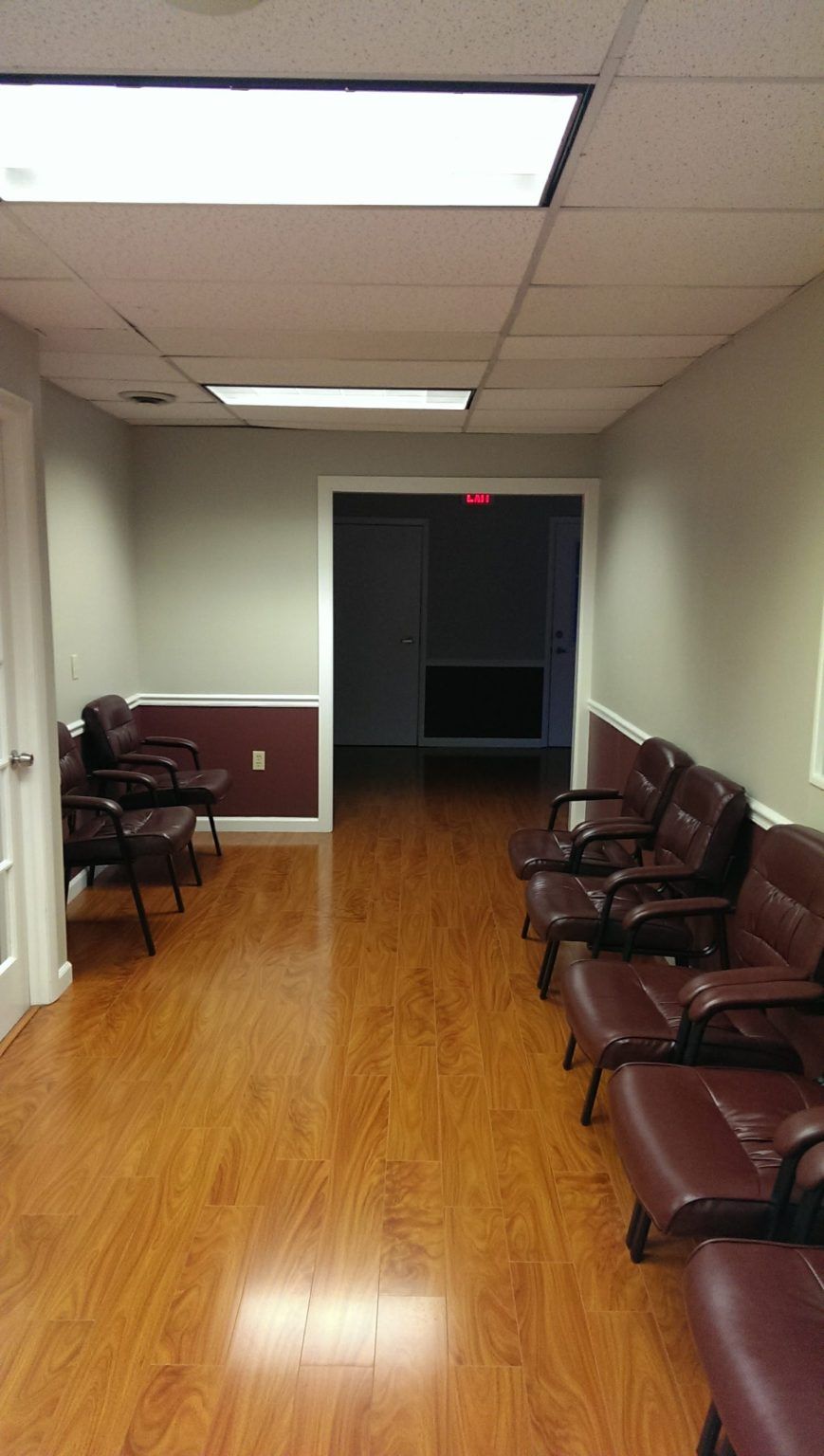 A long hallway with wooden floors and chairs in a waiting room.