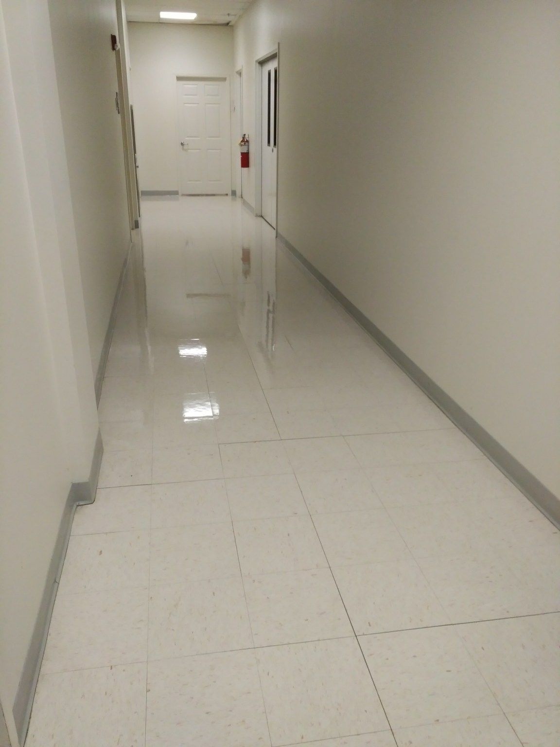 A long white hallway with a fire extinguisher on the wall.