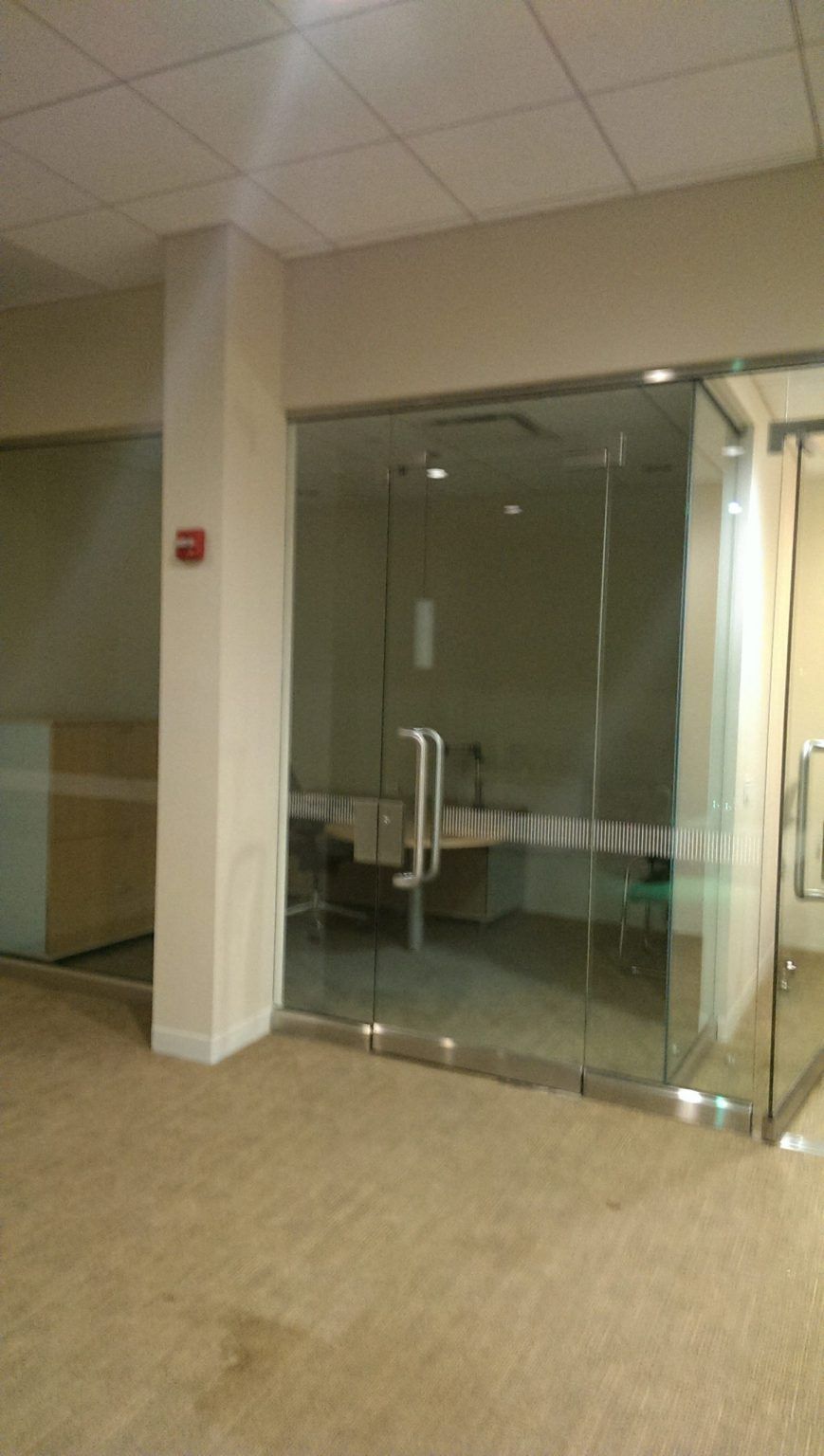 A room with a lot of glass doors and a fire extinguisher on the wall.