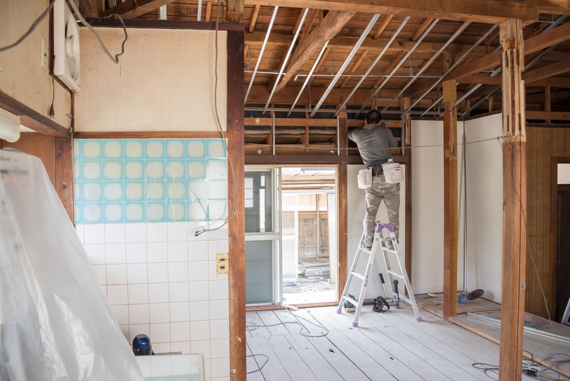 Renovation in progress: a person on a ladder works inside a room with exposed beams and walls.
