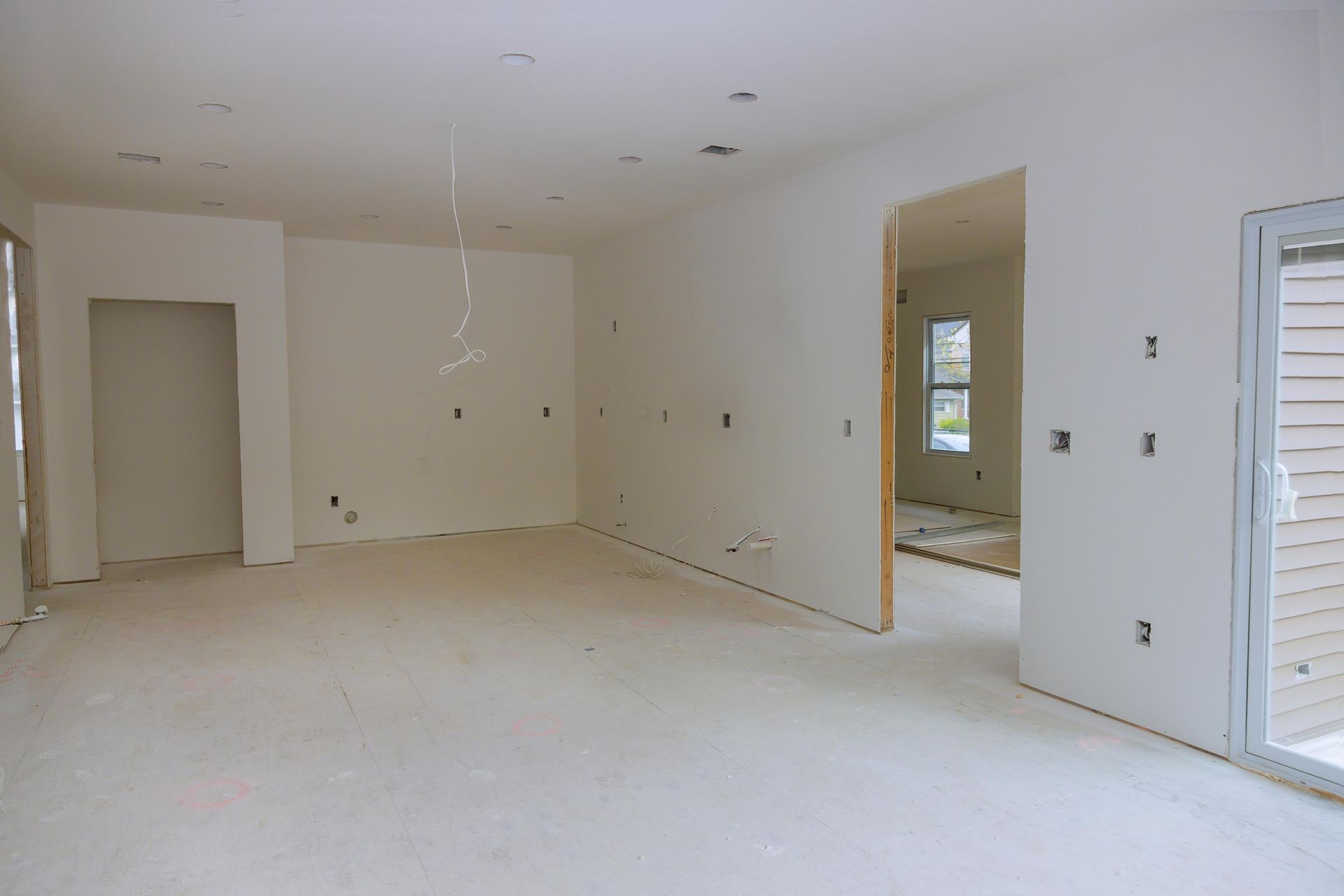Interior of a room under construction, with white walls, exposed wiring, and doorways.