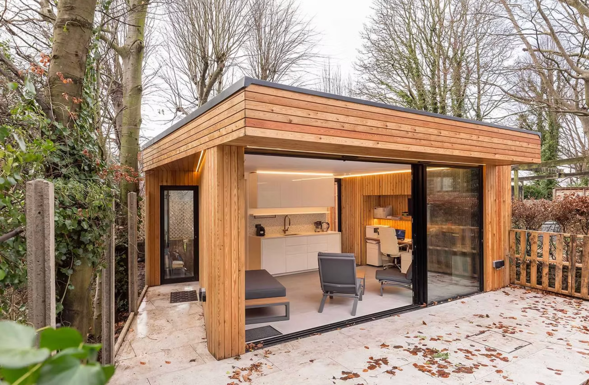 Modern wooden garden room with glass sliding doors, furnished, set in a yard.