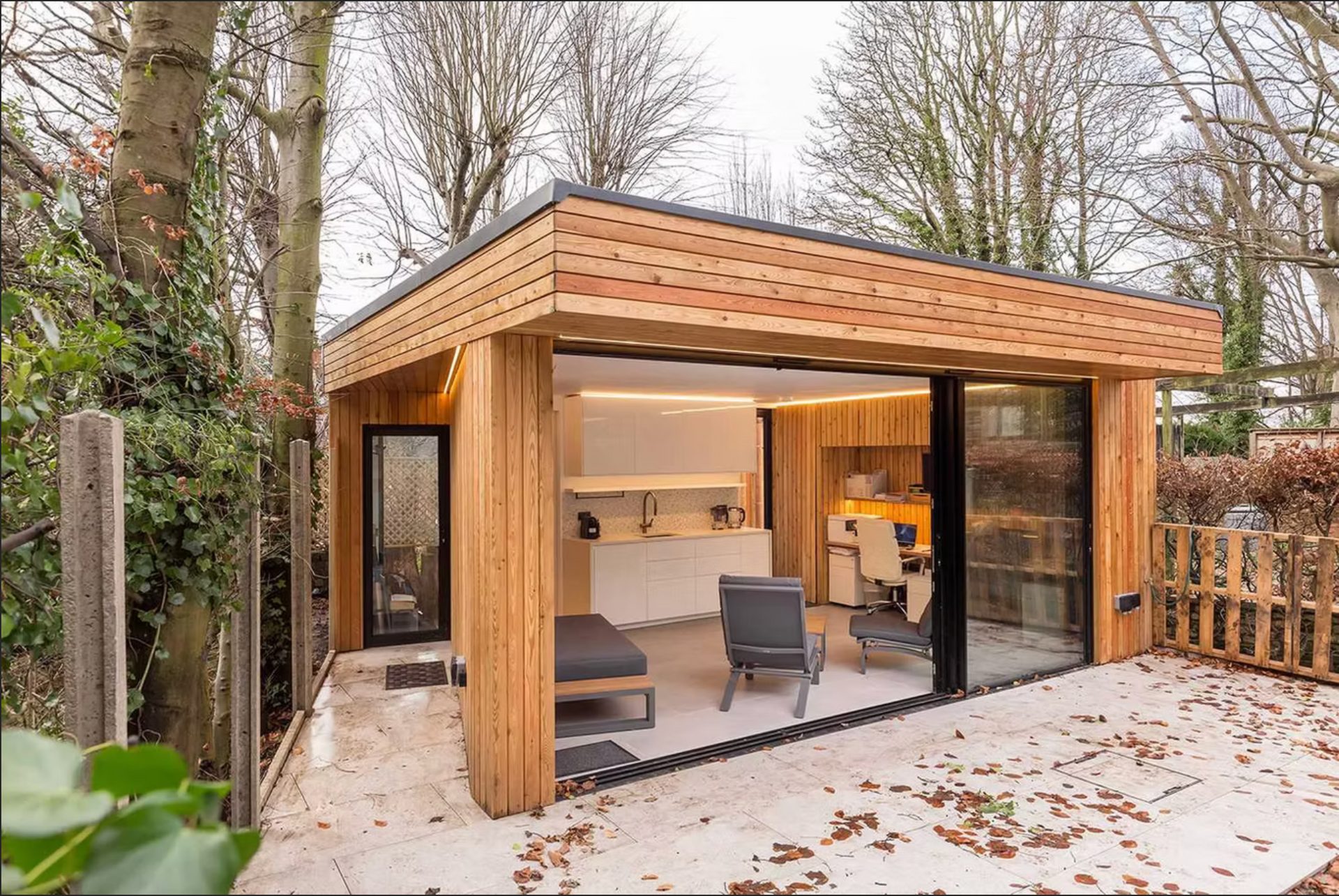 Modern wooden garden office with glass sliding doors, outdoor seating, and interior workspace.