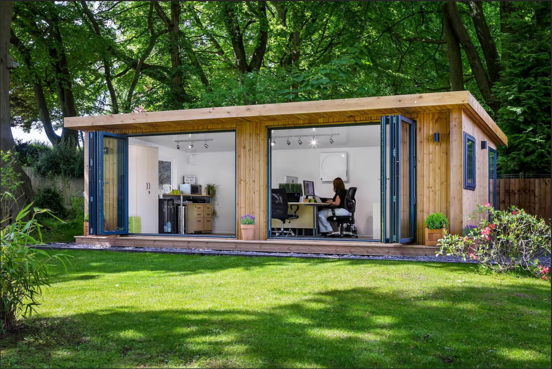 Wooden garden office with large doors open to a grassy lawn, a person working inside.