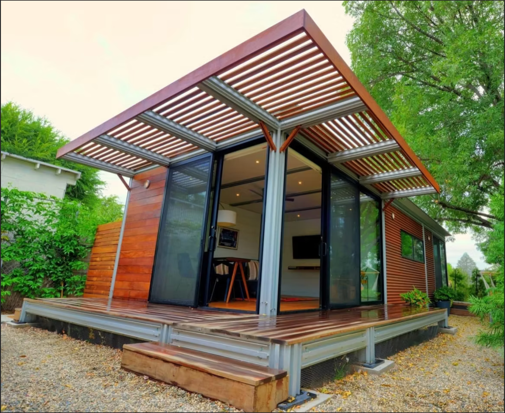 Modern tiny house with wooden siding, deck, and slatted roof. Glass sliding doors open to interior.