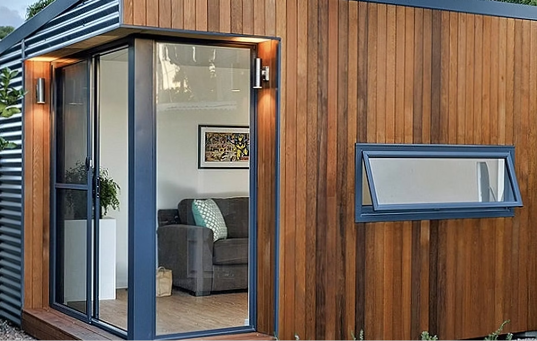 Modern cabin exterior with wooden siding, glass door, small window, and outdoor lighting.