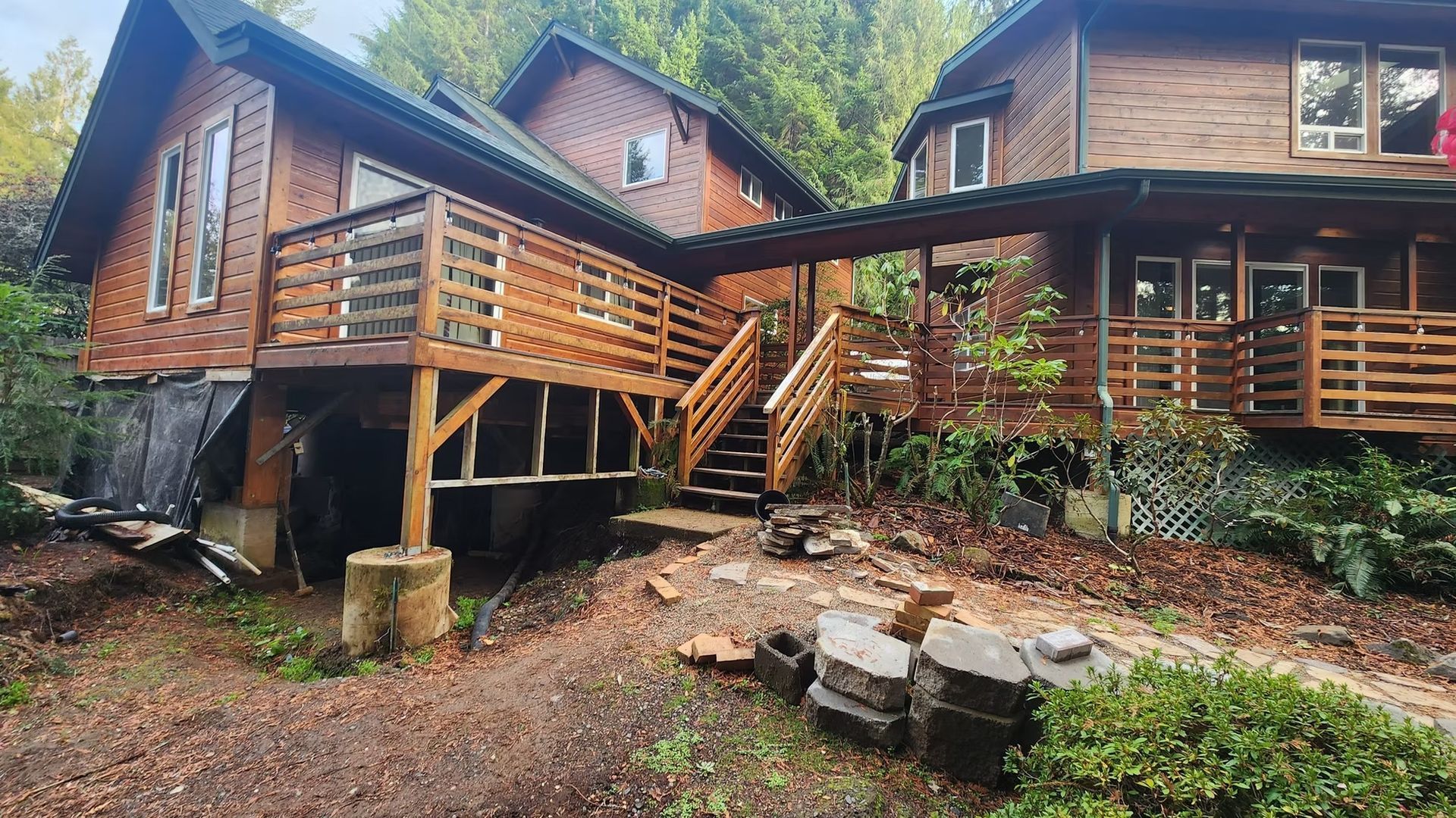 Brown wooden house with deck and stairs in a forest setting.