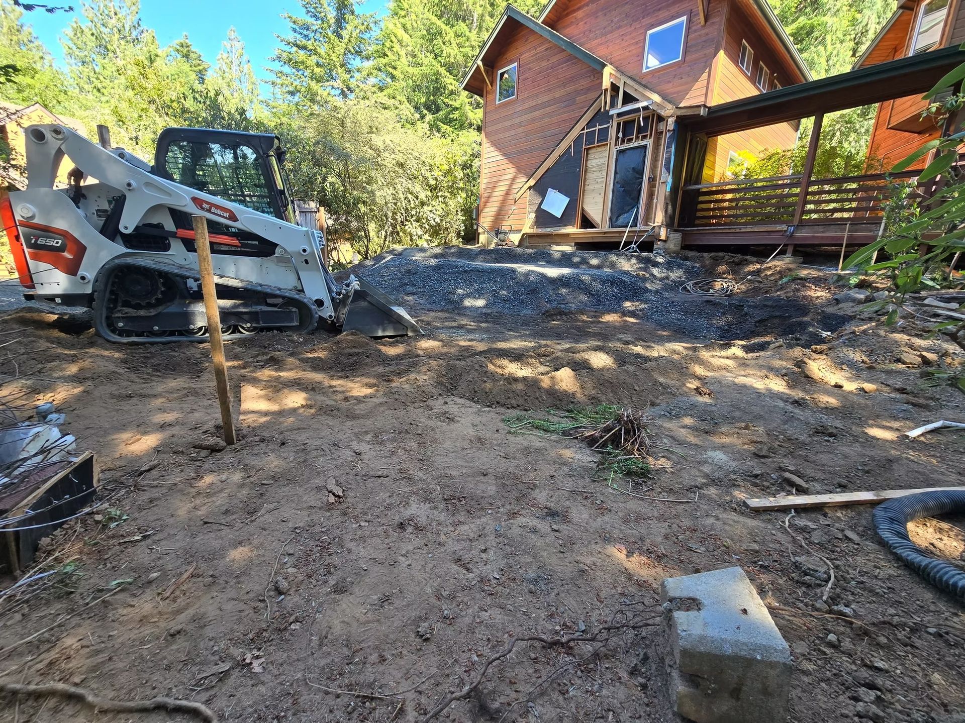 A Bobcat compact track loader grading soil near a house, preparing a construction site.