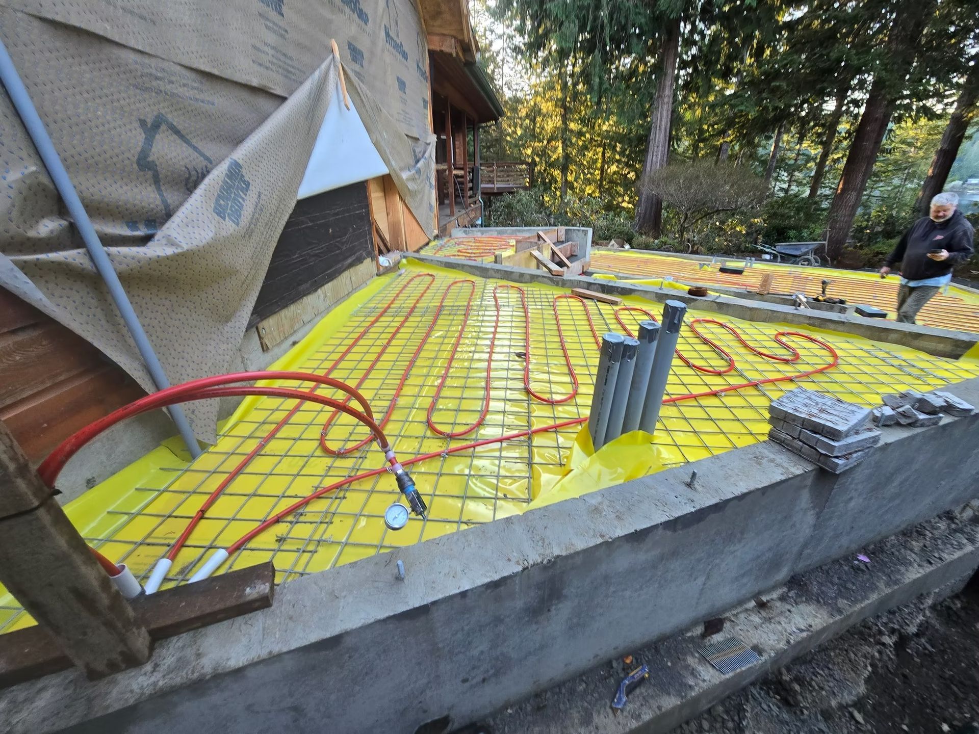 Construction site with radiant floor heating system. Red tubing on yellow underlayment. Person in background.