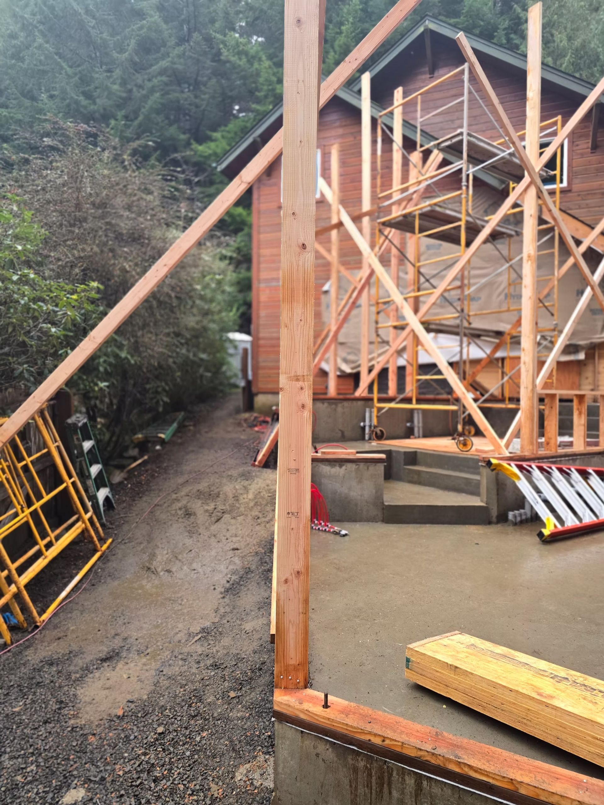 Construction site with wood framing and scaffolding next to a house, on a concrete surface.