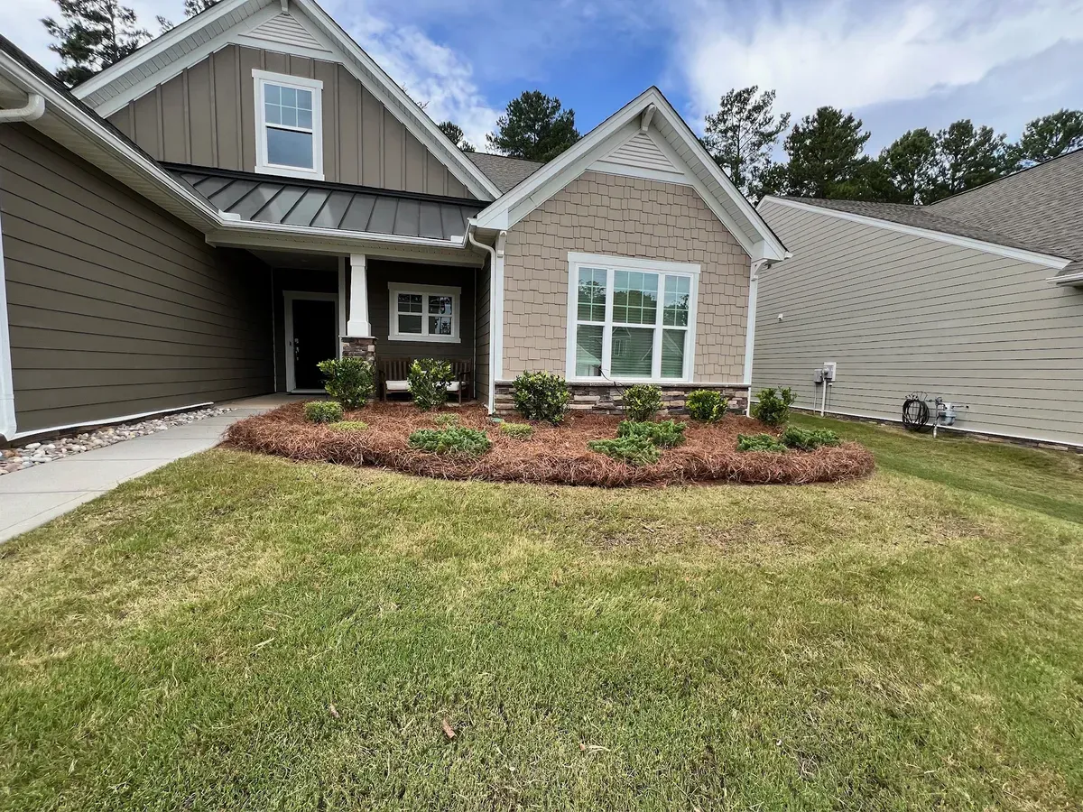 A single-story suburban house with brown horizontal siding, a tan brick facade, a metal roof, and a front mulch garden.