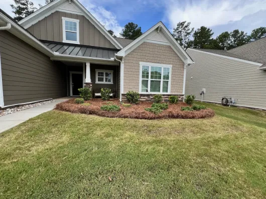A single-story suburban house with brown horizontal siding, a tan brick facade, a metal roof, and a front mulch garden.