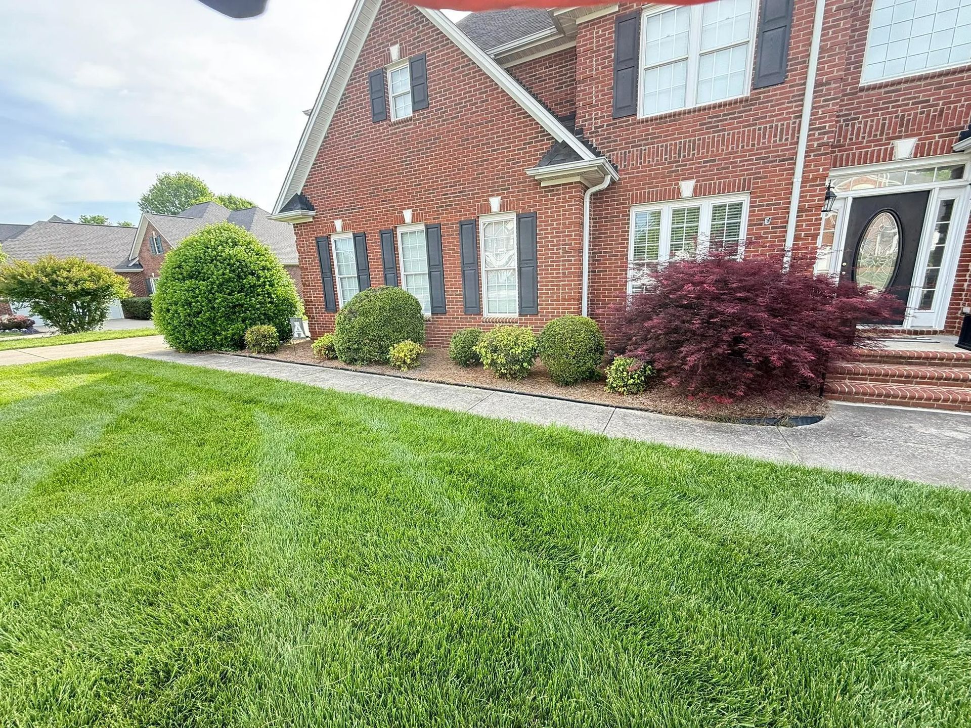 A two-story brick house with a manicured front lawn, landscaped shrubs, and a path leading to the front door.