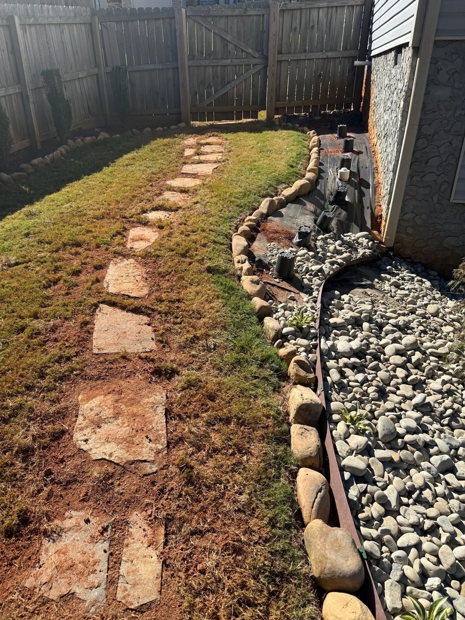 A stone path curves through a grassy lawn beside a rock-filled garden bed bordered by decorative stones next to a house.