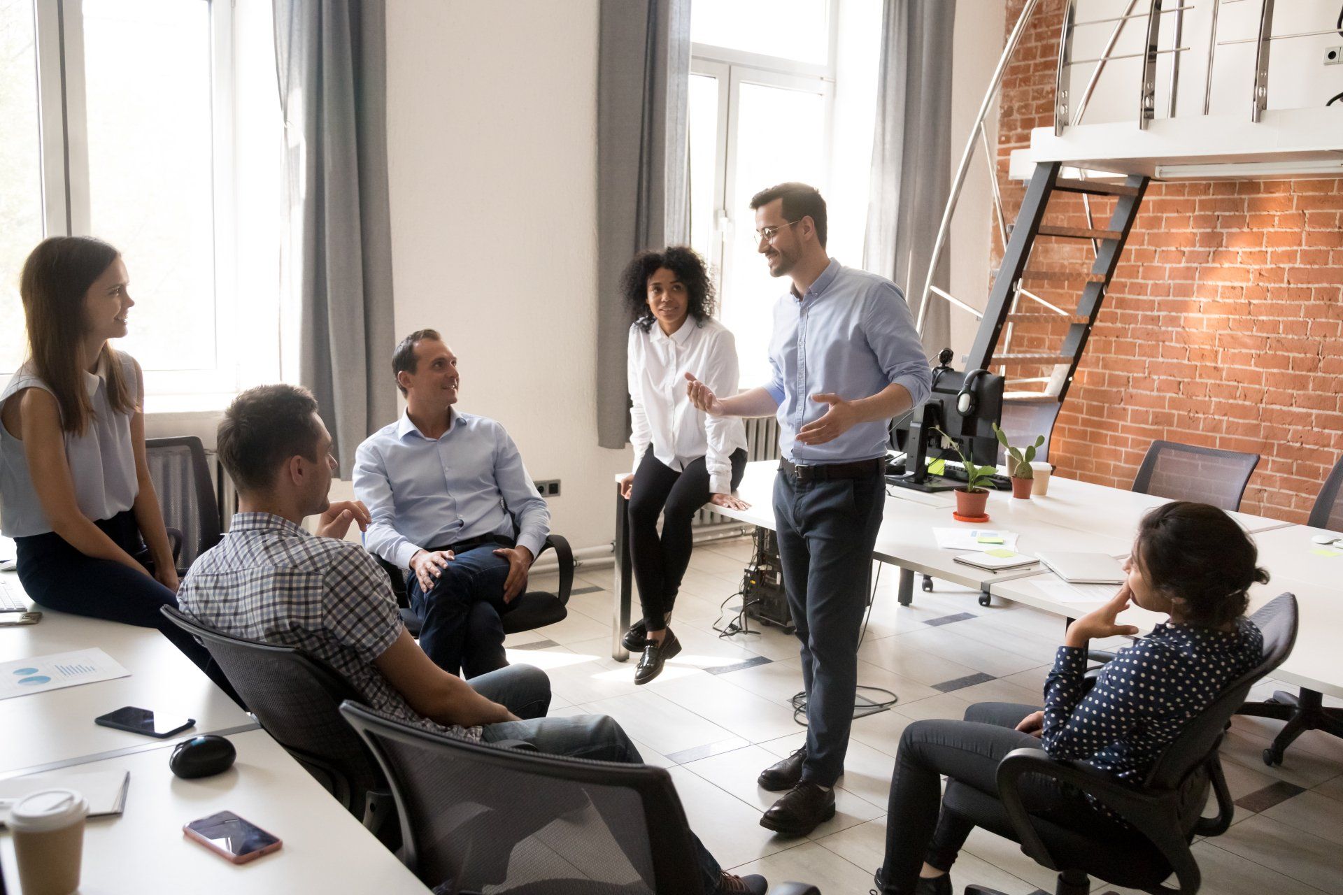 Confident male leader, coach talking with multiracial group of office workers, having good conversation with subordinate, brainstorming, discussing business strategy, ideas, team building activity