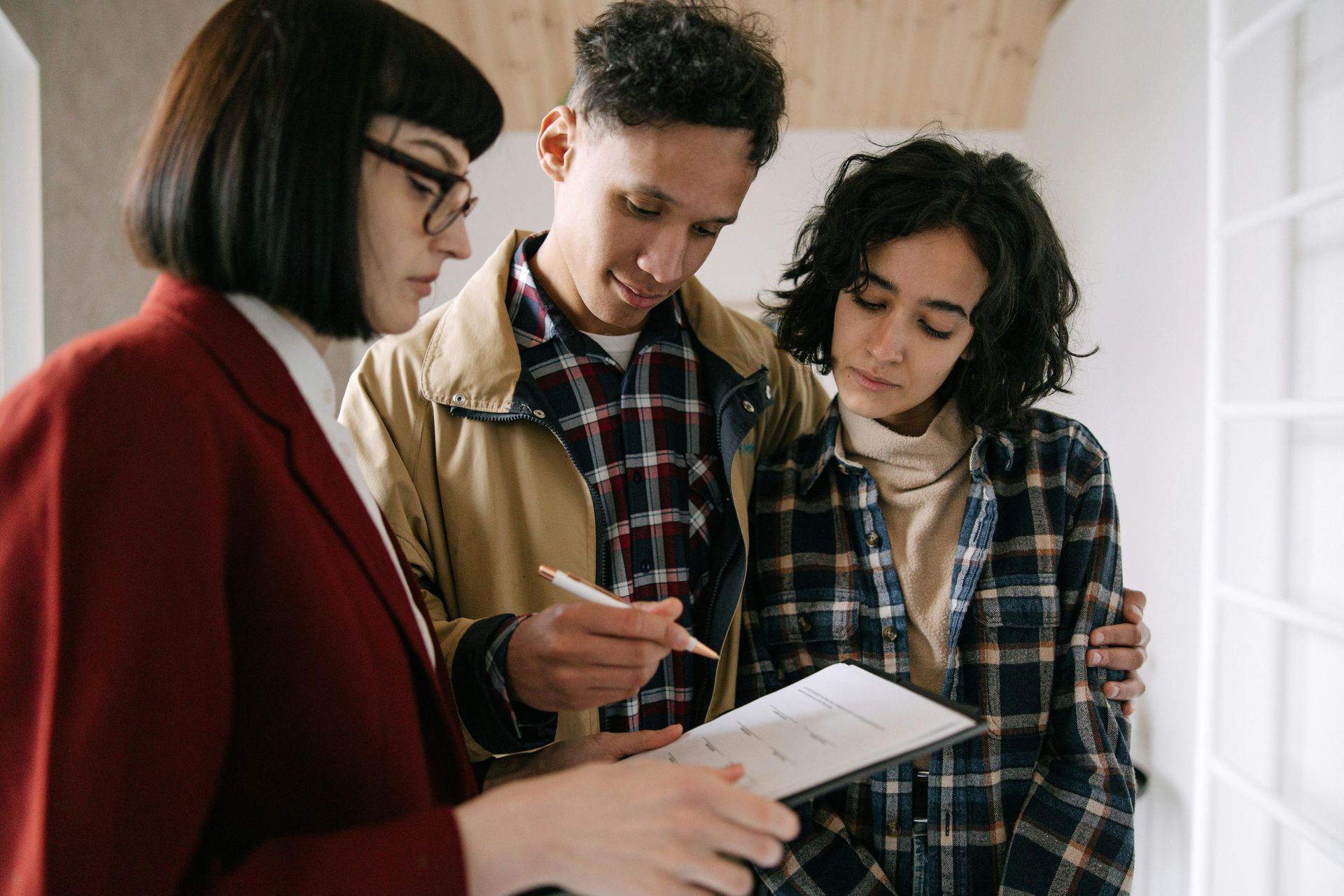 Three people standing together looking at a document held by a person in a red blazer, possibly during a consultation.