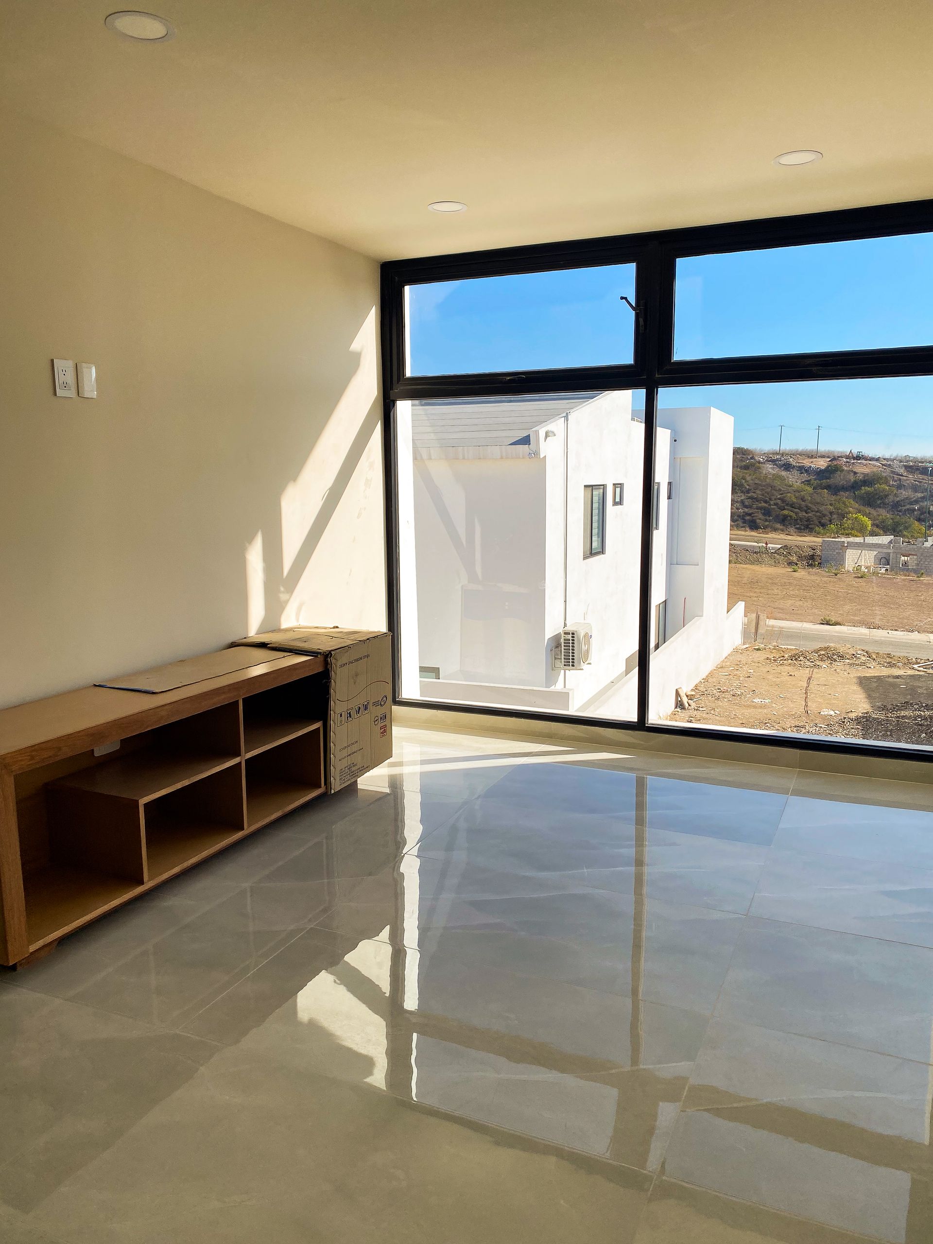 An empty room with a large window and a wooden cabinet