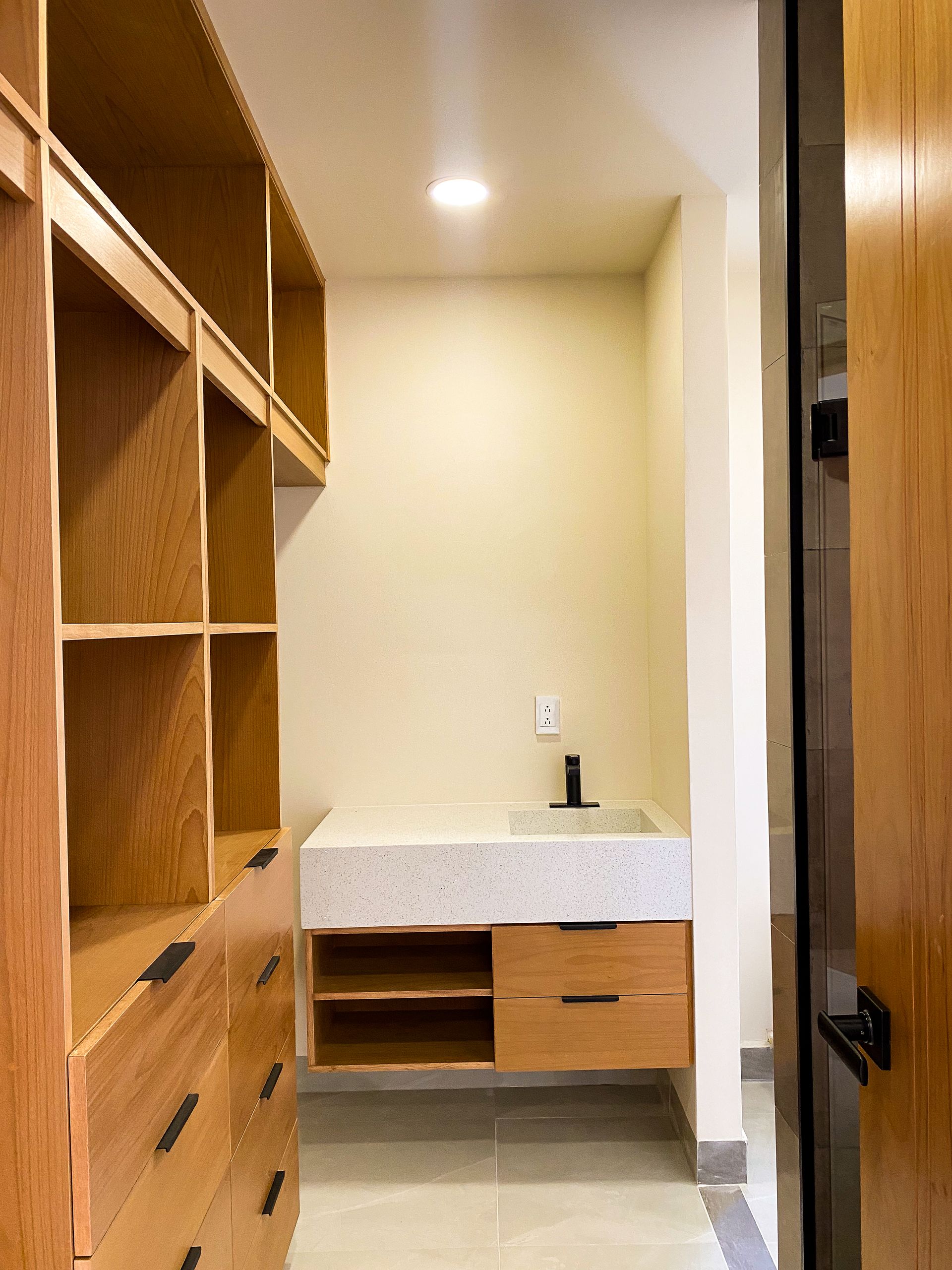 A walk in closet with wooden shelves and drawers and a sink.