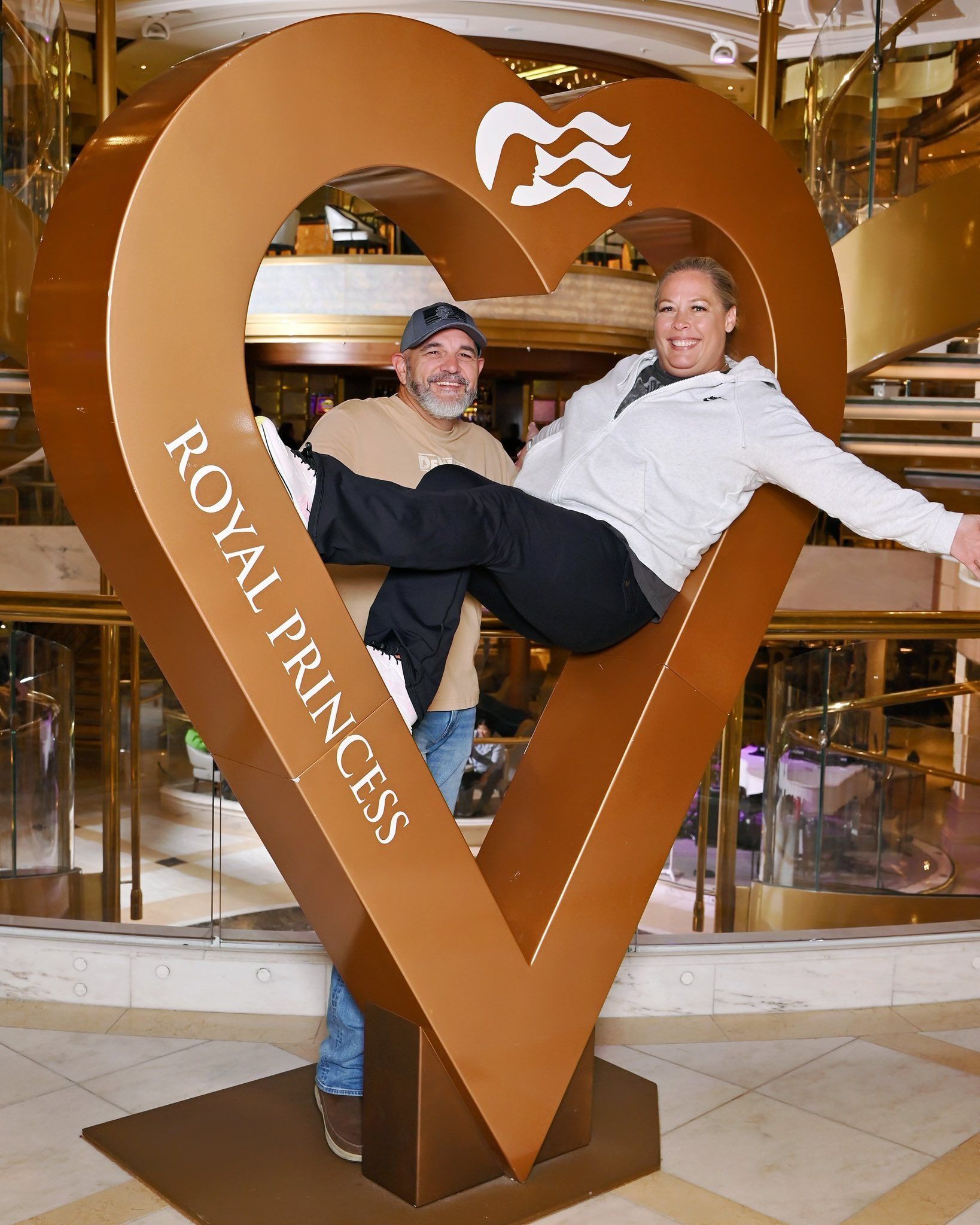 Couple poses for photo inside a gold heart, Princess Cruises logo, 