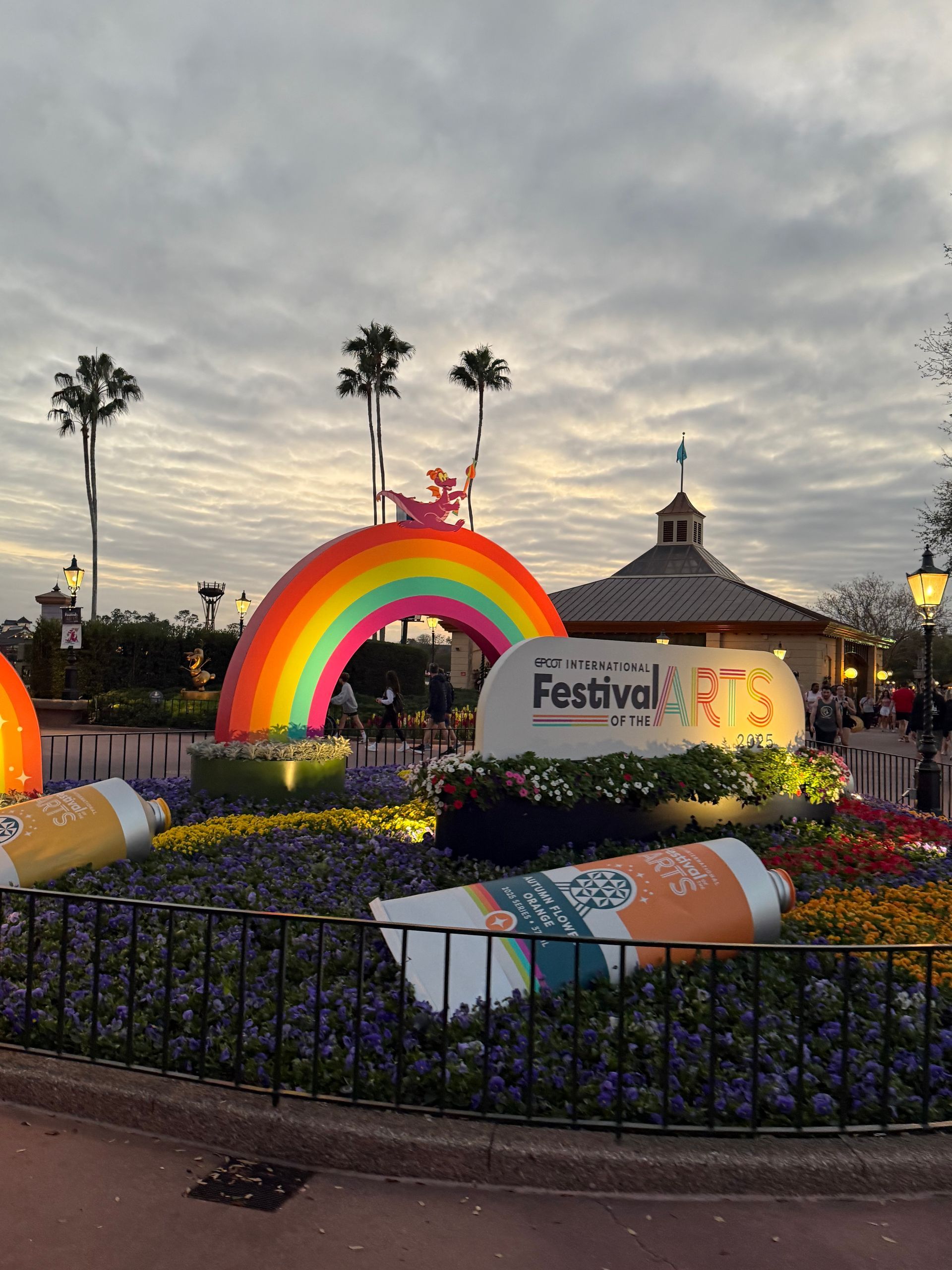 EPCOT Festival of the Arts display with a rainbow, paint tubes, and a sign in front of a building under a cloudy sky.
