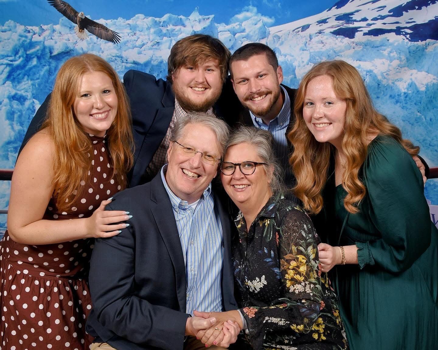 Family smiling, posing together in front of a blue iceberg backdrop, dressed in semi-formal attire.