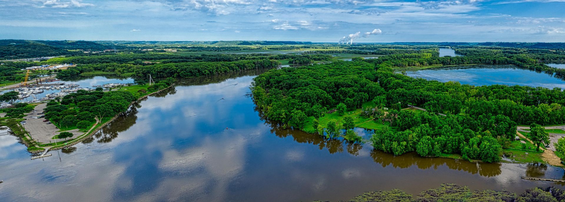 Aerial view of a wide river flowing through a lush green landscape under a cloudy sky.