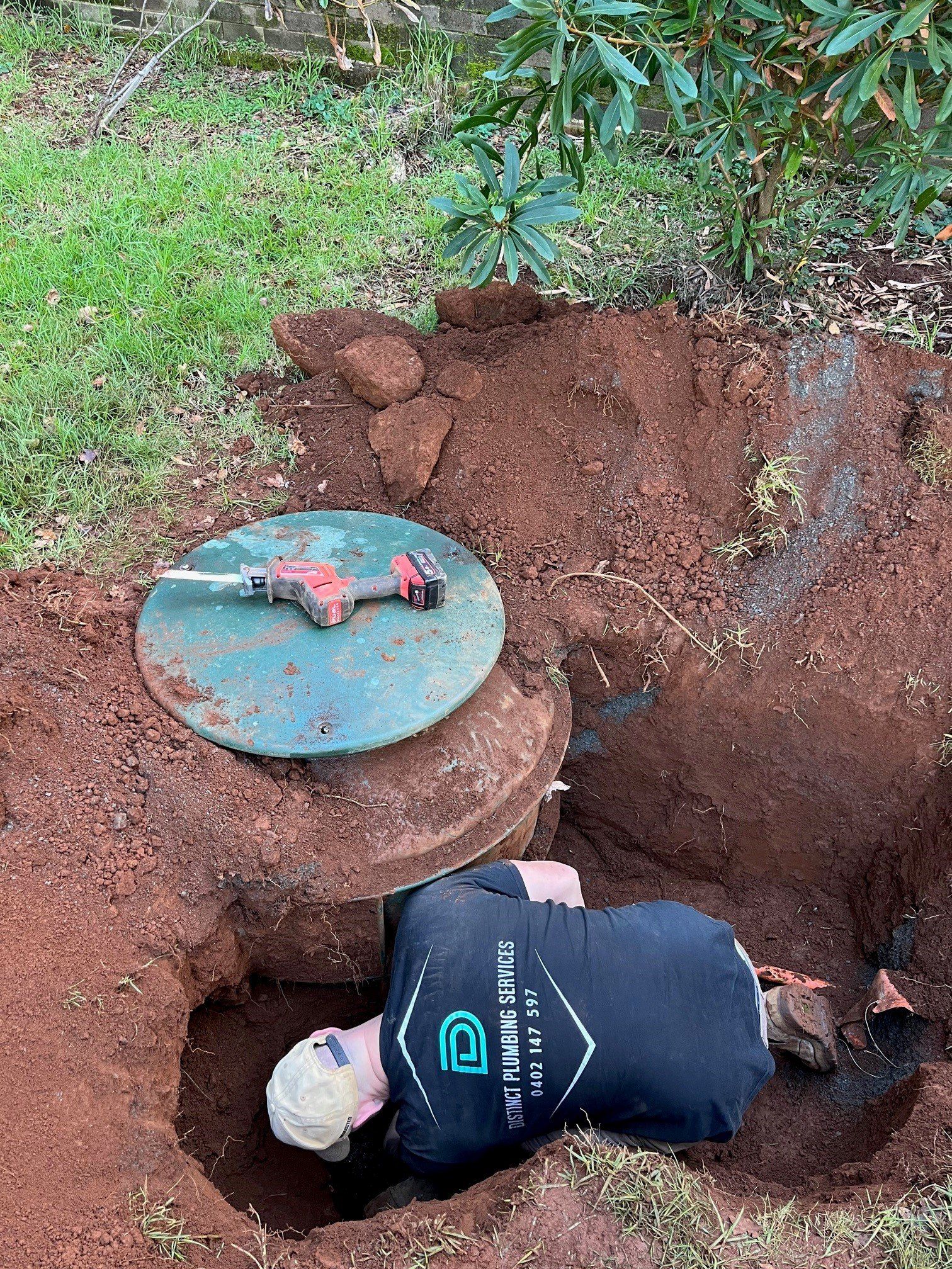 Worker's Hands Hold A Black Pipe Over A Dug Hole On The Ground — Distinct Plumbing Services In Dapto