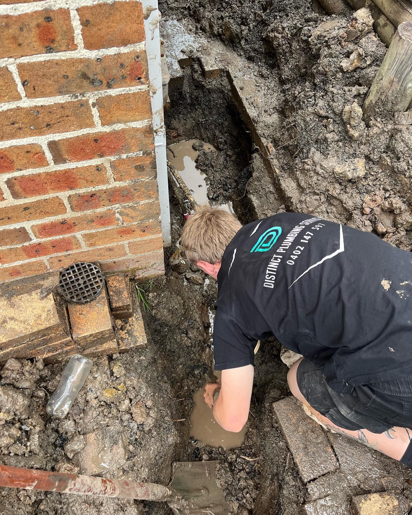 A Person is leaning into a hole in the ground — Distinct Plumbing Services In Kiama, NSW
