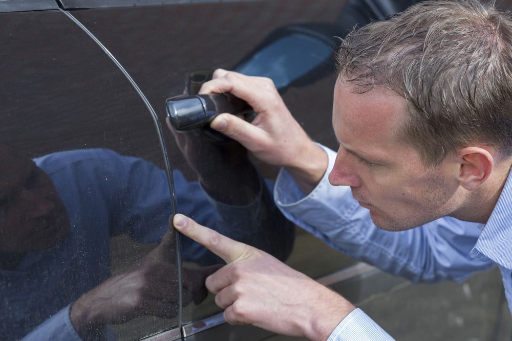 A Man is Pointing at the Door Handle of a Car — Camden Haven Panel Works In Laurieton, NSW