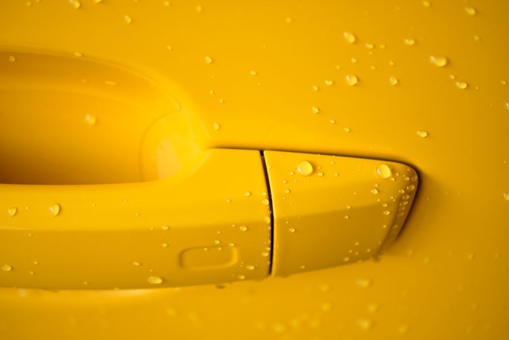 A Close Up of a Yellow Car Door Handle With Water Drops on It — Camden Haven Panel Works In Laurieton, NSW