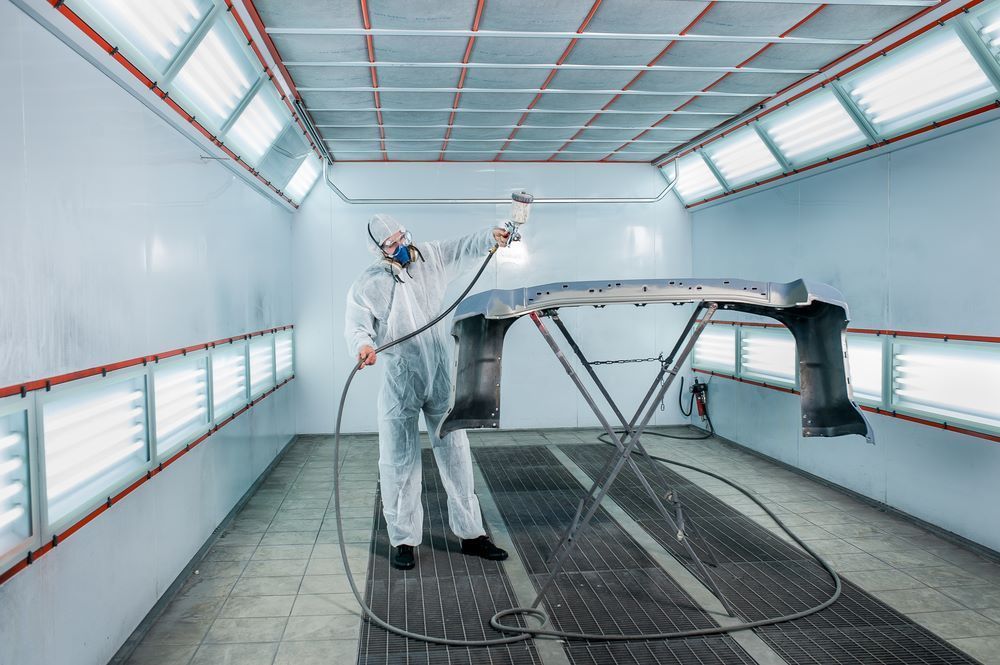 A Man is Painting a Car in a Paint Booth — Camden Haven Panel Works In Laurieton, NSW