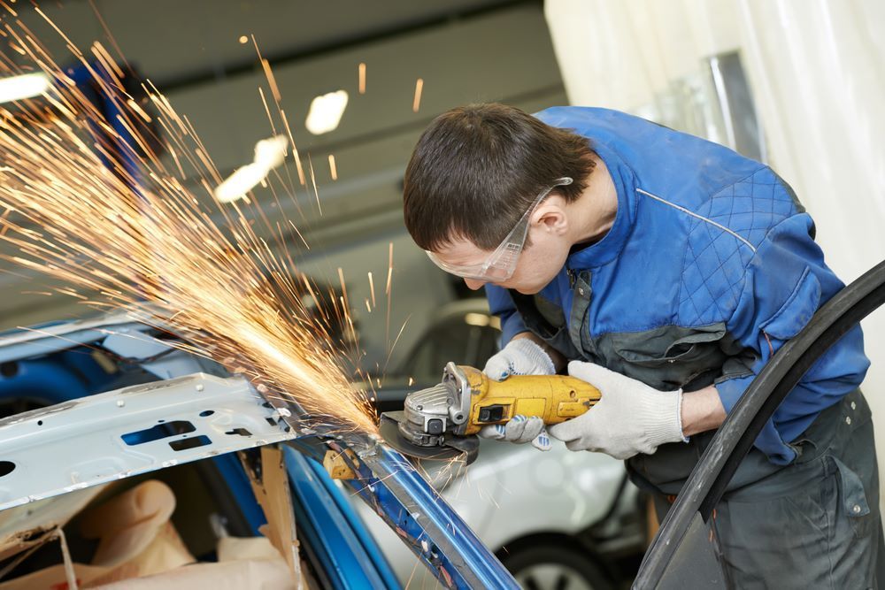 A Man is Grinding a Piece of Metal on a Car — Camden Haven Panel Works In Laurieton, NSW