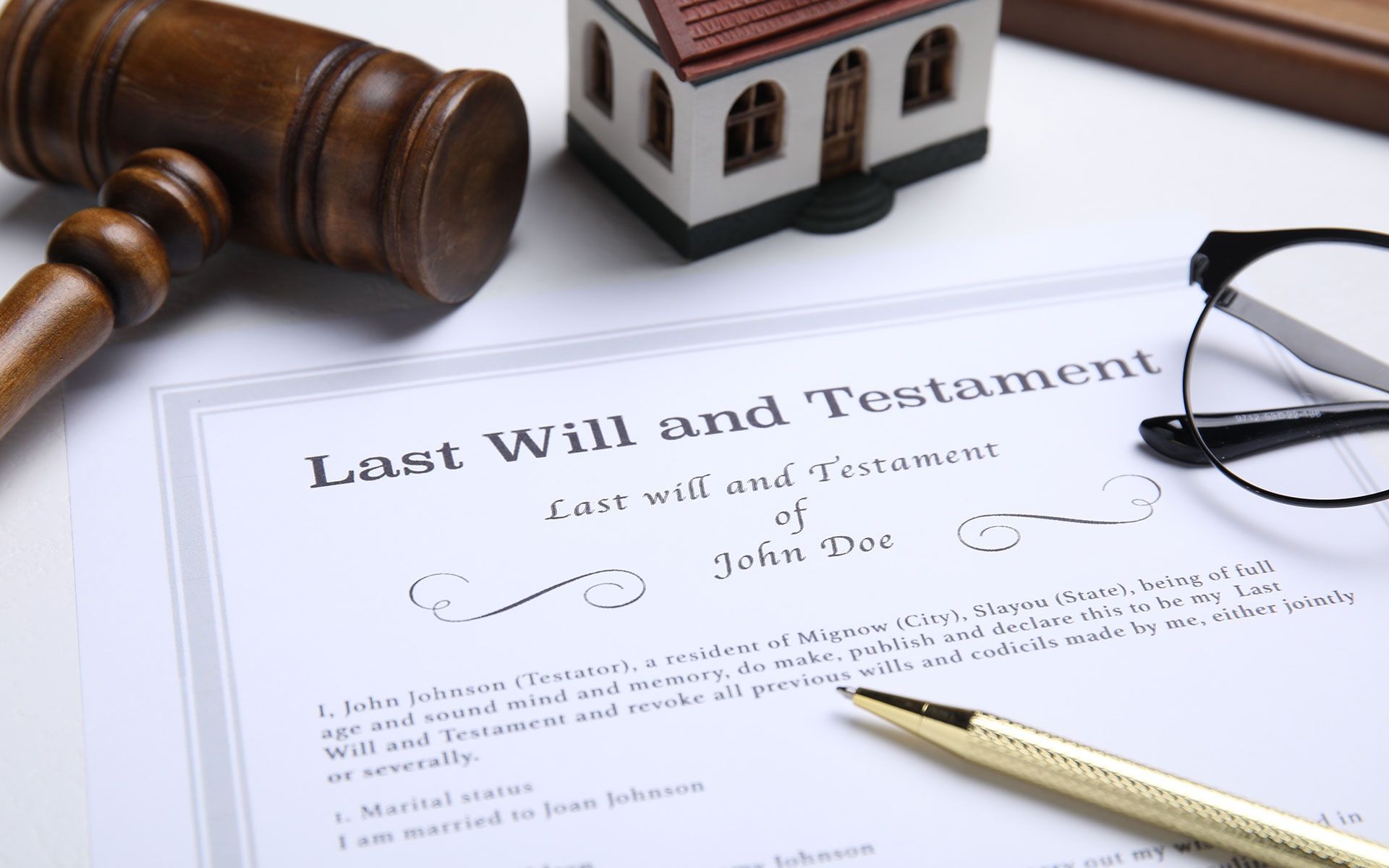 Last Will and Testament document with gavel, model house, glasses, and pen on white surface.