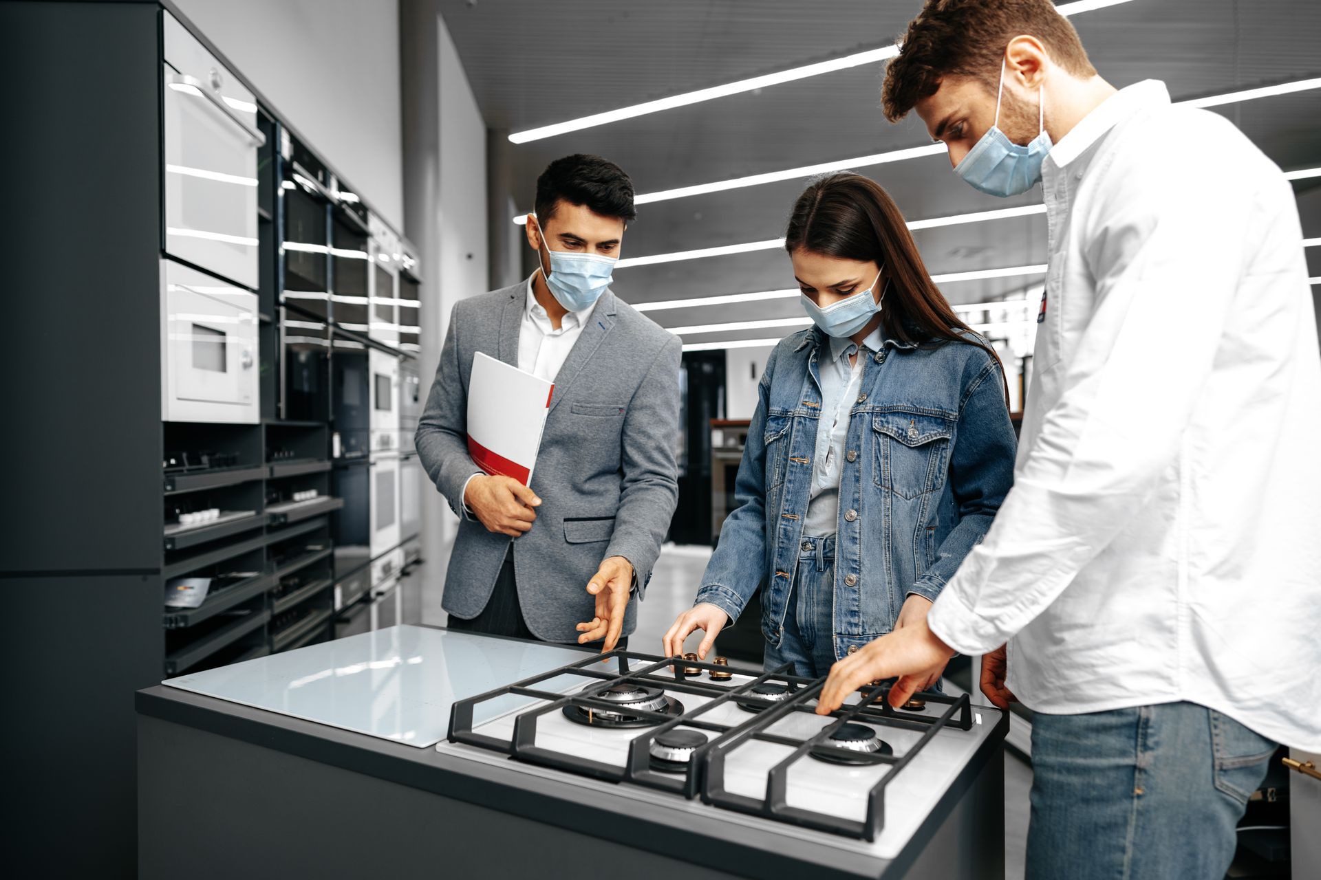 a man and a woman wearing masks are looking at a gas stove in a store .