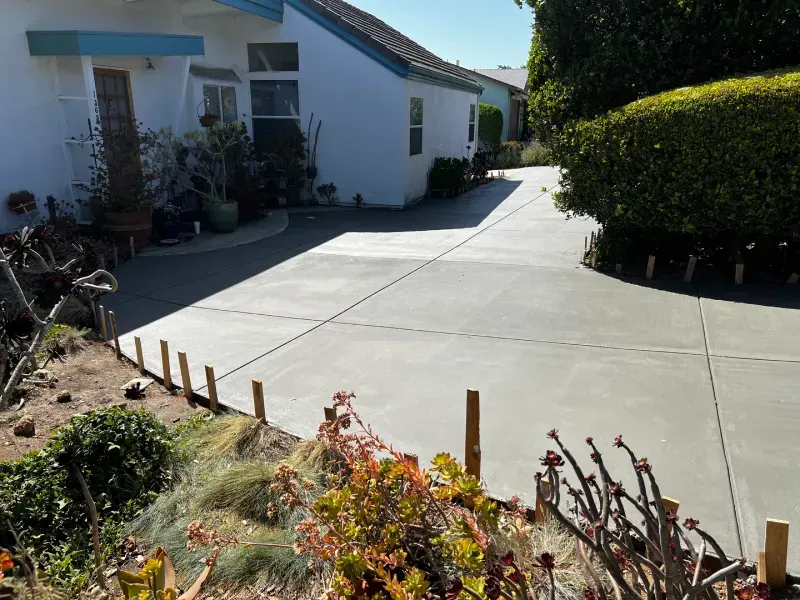 Freshly poured concrete driveway in front of a white house with landscaping.