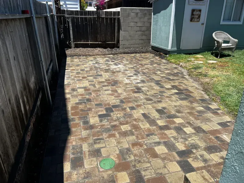 Brick patio in a backyard with a fence, shed, and grass.