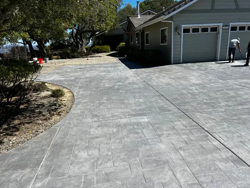 Gray stamped concrete driveway leading to a house with a garage; two people stand nearby.