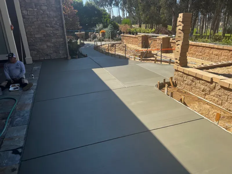 Freshly poured concrete walkway, next to a stone wall. A worker sits nearby.