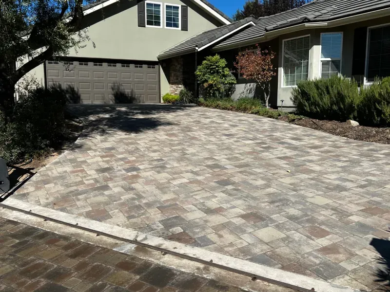 Brick paver driveway in front of a house with a brown garage door and landscaping.