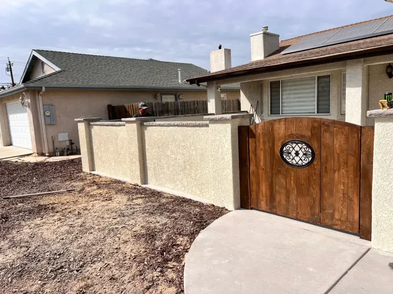 Wooden gate in a stucco wall, leading to a house with solar panels.