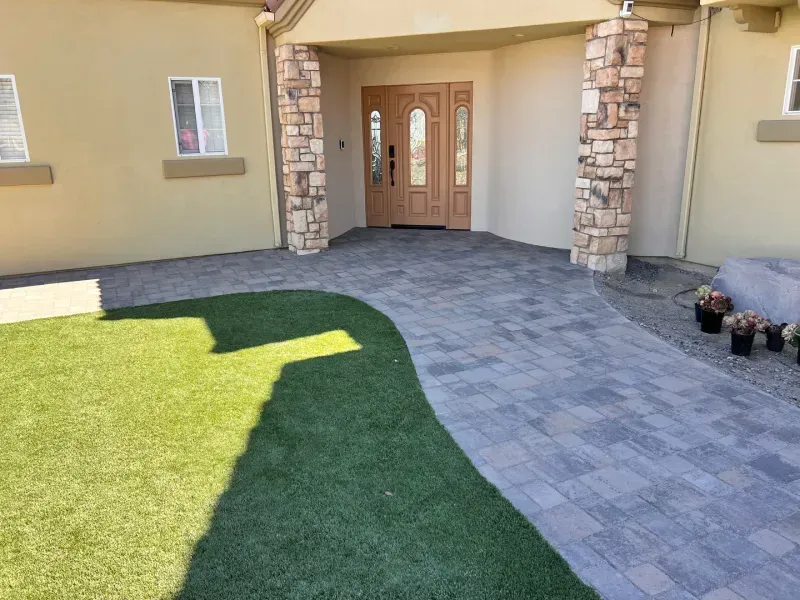 Paver walkway leading to a house entrance with stone columns and a lawn area.