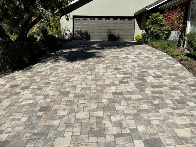 Brick driveway leading to a two-car garage. Driveway is brown and gray brick, garage door is brown.
