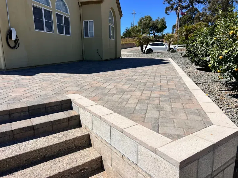 Stone patio with steps, retaining wall, and tan building in the background. Sunny day.